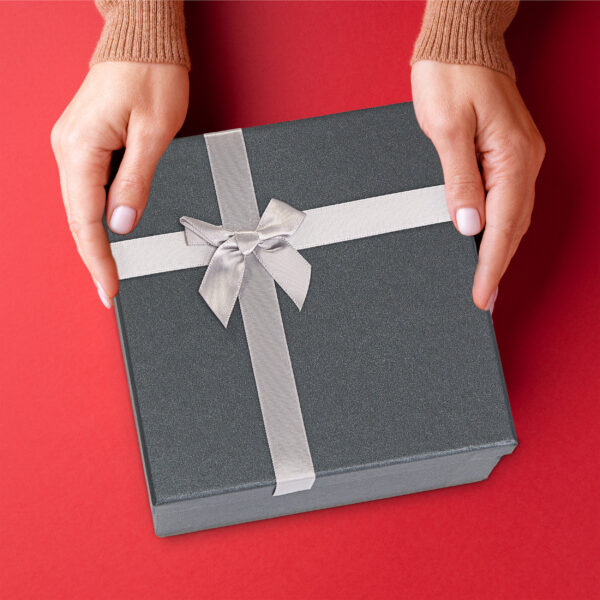 Female’s hands holding red gift box on red background.